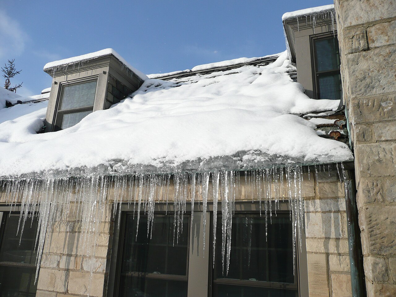 Visible ice dam with icicles along the eave of a snow-covered roof