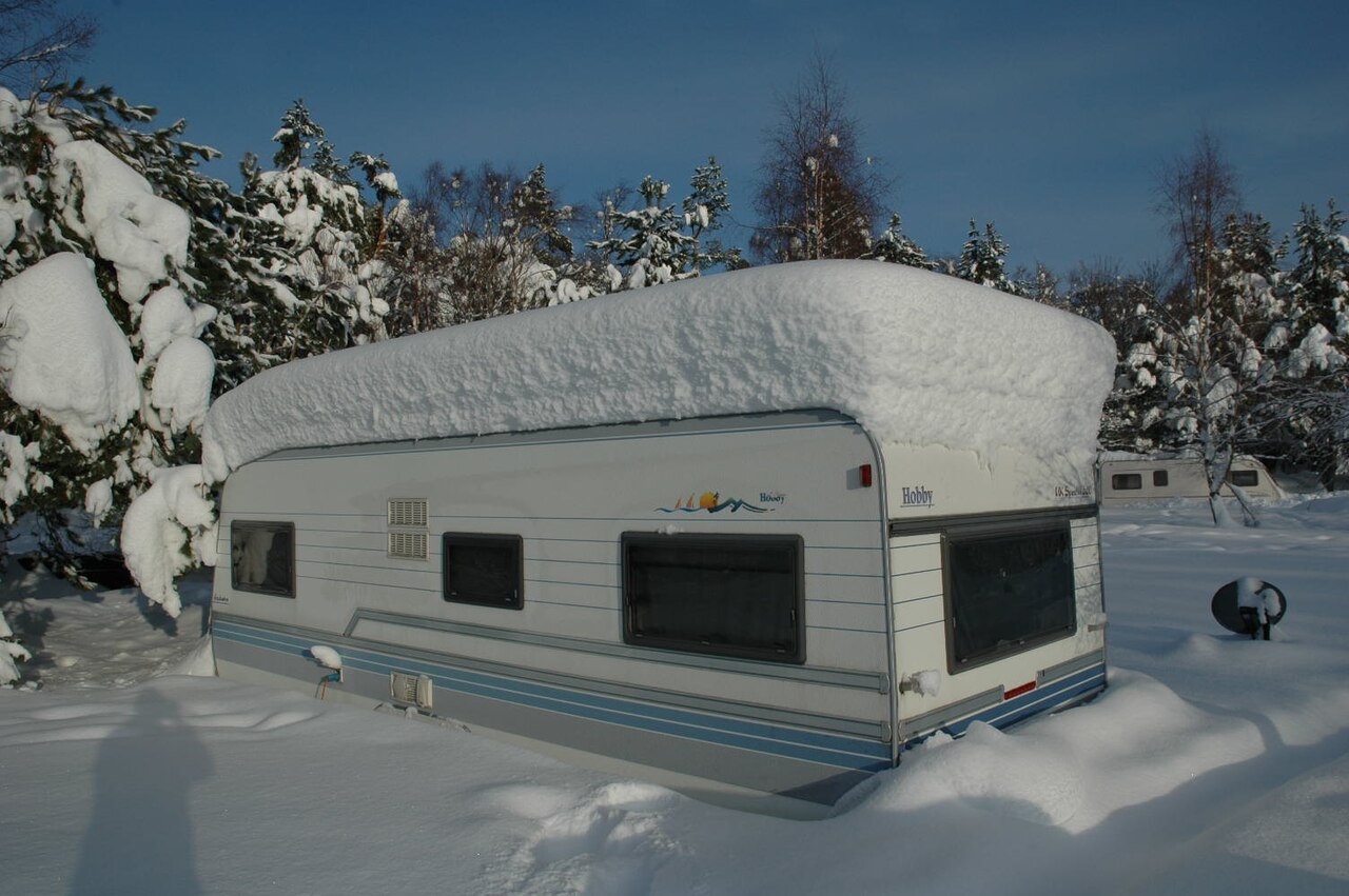 A camper parked in deep winter snow with snow accumulated on its roof